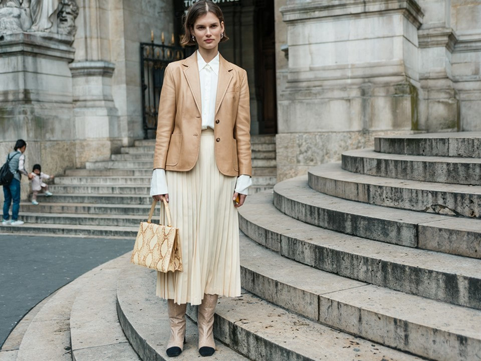 Fall clothing fashion - young professional in shades of cream, long pleated cream skirt, creal long sleeve top, leather jacket in light camel color with ankle books to match - Luxury apartments in lafayette la